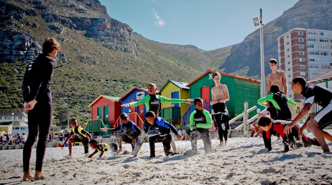 A Projects Abroad volunteer teaches surfing in South Africa by showing children how to stand on a surfboard Children learn to stand on their surfboards through volunteer surf coaching in South Africa